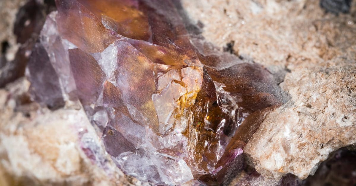 Cristal de fluorita violeta y ámbar con planos de rotura lisos sobre la roca